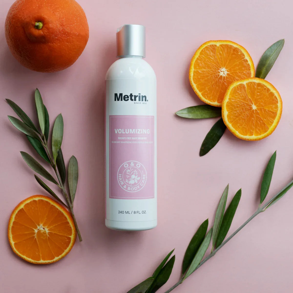 Metrin volumizing hair shampoo bottle with oranges and leaves on a pink background