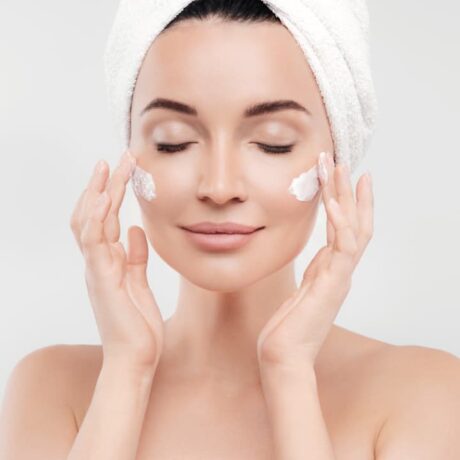 woman applying cream to cheeks with towel wrapped around hair